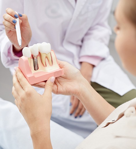 Woman holding sample implant with dentist pointing with pen