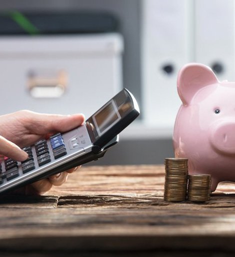 Close up of patient using a calculator next to piggy bank and coin stack