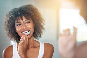 Woman with curly brown hair brushing her teeth at a mirror