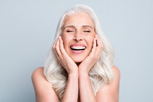 Woman with white hair smiling and holding both hands to cheeks