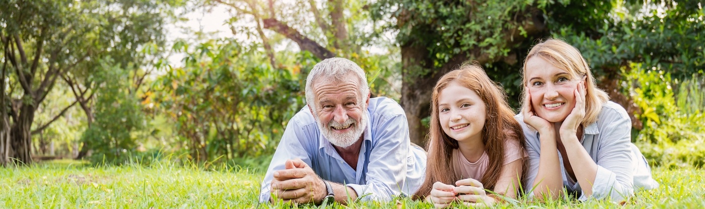 Three generations of a smiling family laying in grass after visiting dental office in Allen