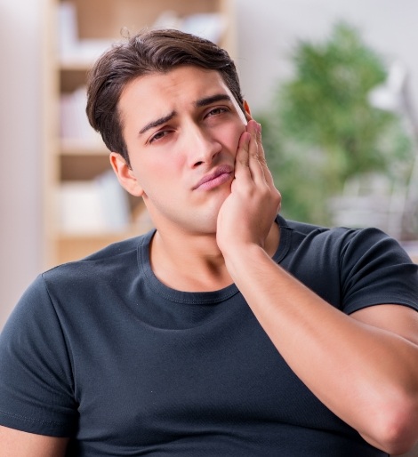 Man wincing in pain while holding the side of his jaw