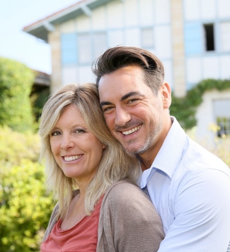 Man and woman smiling and hugging in their yard