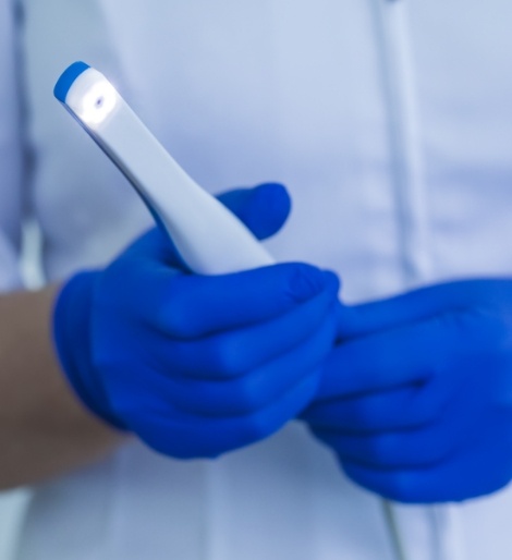 Gloved hands holding a white pen like intraoral camera