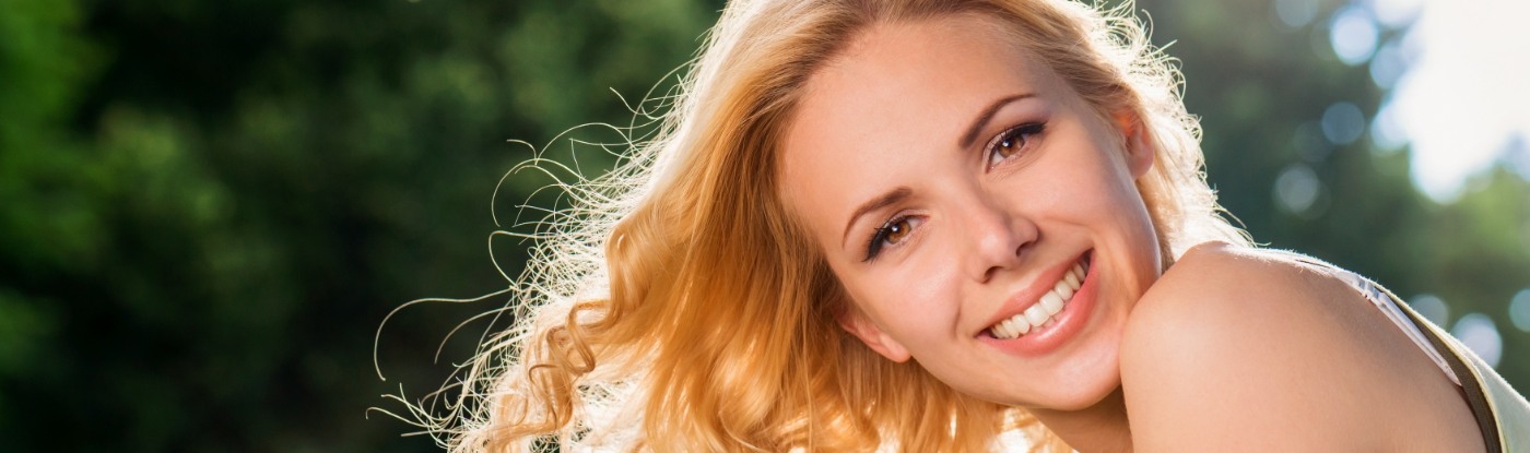 Blonde woman grinning outdoors after seeing cosmetic dentist in Allen