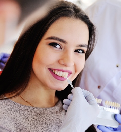 Dentist holding a veneer next to a smiling patients teeth