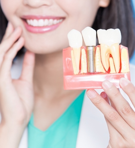 Smiling dentist holding a model of a dental implant