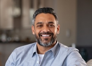 Man in pale blue collared shirt smiling on couch