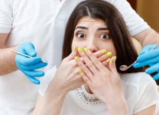 Woman covering her mouth and looking fearful in dental chair