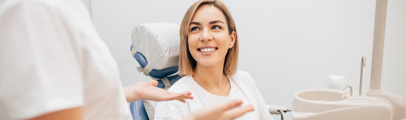 Woman in dental chair smiling while listening to her dentist talk