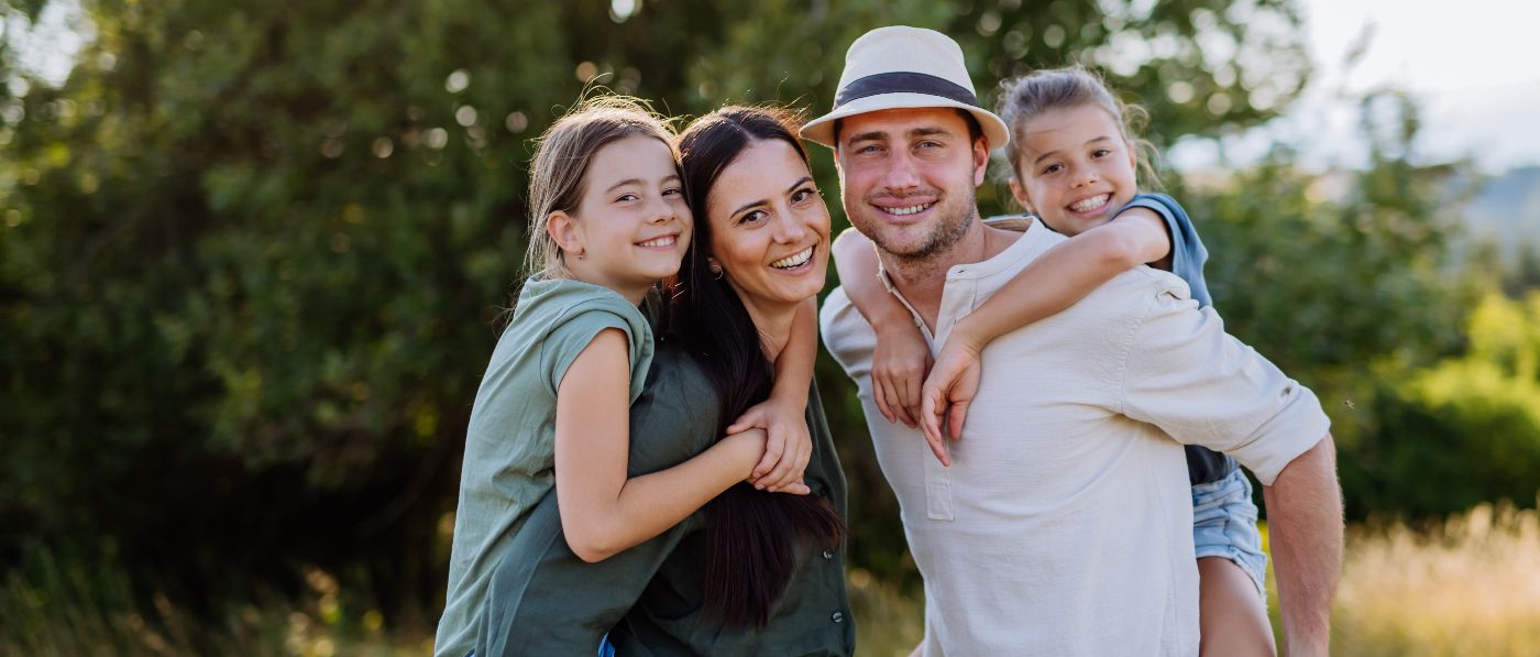 Family of four smiling outdoors after seeing their dentist in Allen