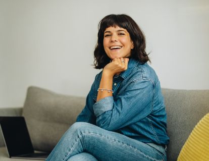 Smiling woman in jeans and denim jacket sitting on couch