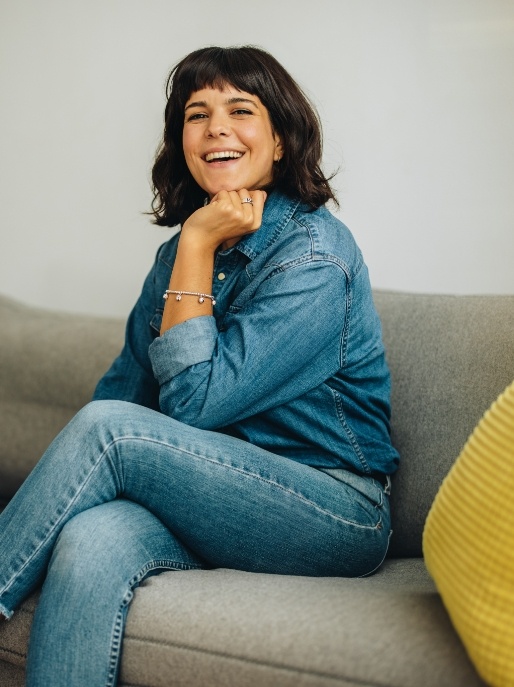 Smiling woman in jeans and denim jacket sitting on couch