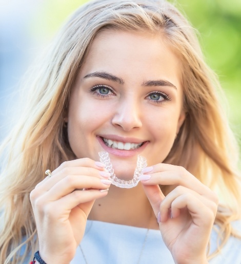 Blonde woman holding a clear aligner near her teeth