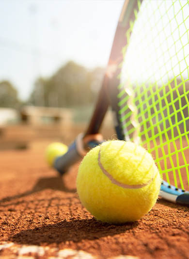 Tennis ball and racket laying on the ground at a tennis court