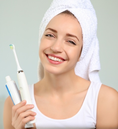 Smiling woman with her hair in a towel holding a toothbrush and tube of toothpaste