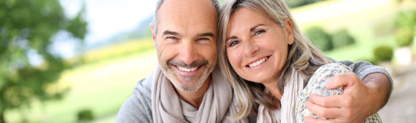 Older man and woman smiling and hugging outdoors after restorative dentistry in Allen