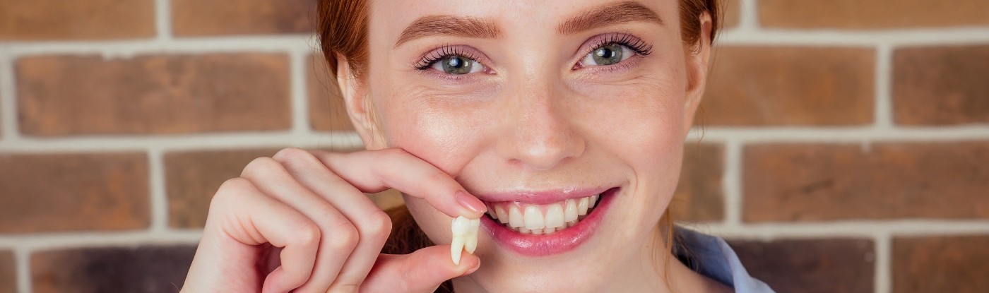 Smiling woman holding a tooth after a tooth extraction